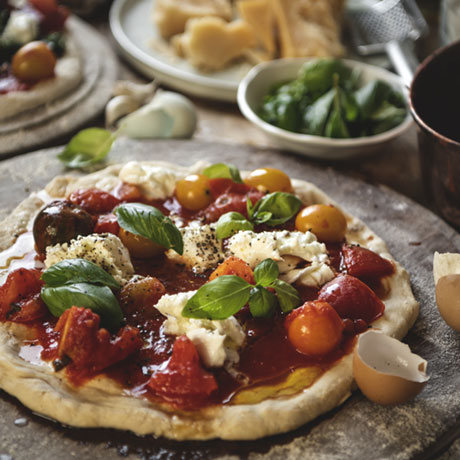 Primer plano de una pizza de queso, tomate y albahaca.